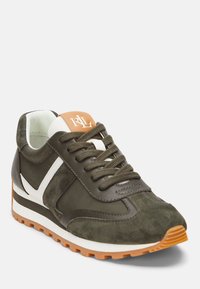 Mockasin och tygsneaker i olivgrön med vita detaljer, bruna snören och en tan-logopatch på tungan. Vit mellansula, texturerad orange sula.