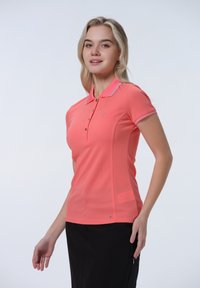 Korálová polo košile vyrobená z lehkého materiálu s krátkými rukávy, tříknoflíkovou légou a kontrastním lemem kolem límce. Logo viditelné na hrudi.