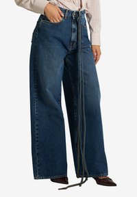 Jeans a gamba larga in denim blu scuro con vita alta, dotati di chiusura frontale con zip e bottone, e un dettaglio aggiuntivo con fiocco.