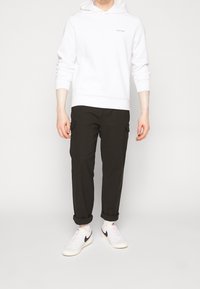 Witte hoodie met Calvin Klein-logo, zwarte cargo pants met zijzakken en witte schoenen met zwarte accenten. Glad materiaal en een relaxte pasvorm.