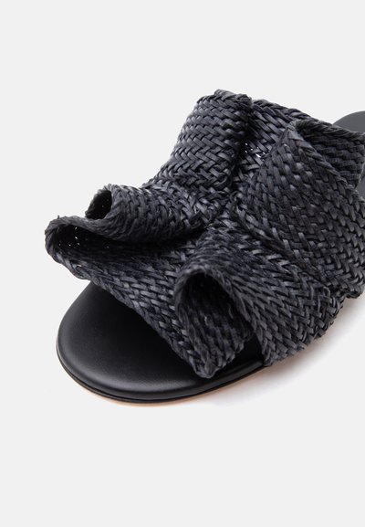 Μαύρο πλεκτό δερμάτινο σανδάλι-slide με φαρδιές επικαλυπτόμενες λουρίδες και ανοιχτό δάχτυλο σε απλό φόντο.