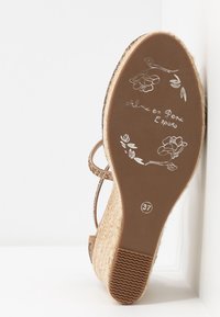 Sandalia de cuña con suela texturizada de yute, color marrón claro y una correa de tobillo con abalorios. Presenta diseños florales en la planta interior y marcado de talla 37.