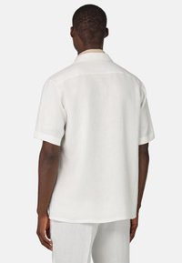 Camicia in lino a maniche corte bianca con una silhouette rilassata, caratterizzata da un colletto classico e una trama sottile. La vista posteriore mostra linee pulite.