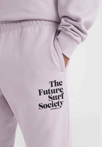Lila sweatpants met een zachte textuur, voorzien van een zijzak en een zwarte grafische print met de tekst "The Future Surf Society."