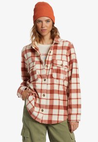 Red and white plaid flannel shirt with button closures, two front pockets, and a soft texture, paired with an orange knit beanie.