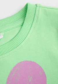 Jasnozielona sweatshirt z okrągłym dekoltem i prążkowanym kołnierzem; na przodzie znajduje się duża, wyblakła, różowa okrągła grafika. Miękki materiał bawełniany.