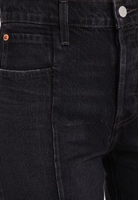 Jeans de pana oscura con un corte clásico, herrajes plateados, un bolsillo frontal y detalles de costura sutiles. La tela tiene un acabado ligeramente texturizado.