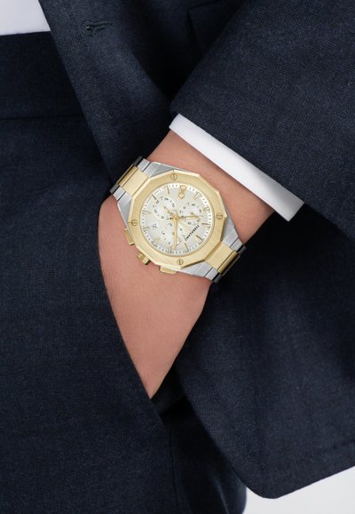 Orologio da polso in argento e oro con cassa ottagonale, cinturino metallico e quadrante argento chiaro con dettagli cronografici e sei indicatori.