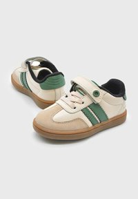 Coppia di sneaker per bambini beige e verdi con cinturino in velcro e lacci su suole di gomma marrone, esposte su uno sfondo chiaro e semplice.
