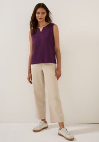 Top viola senza maniche con scollatura a V, abbinato a pantaloni larghi color crema e sneakers bianchi con accenti beige.