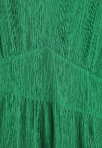 Grüner, zerknitterter Stoff mit vertikalen und horizontalen Mustern, einem strukturierten Finish und geschichteten Designelementen.