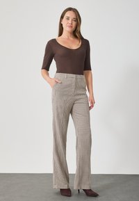 Haut marron ajusté à manches longues associé à un pantalon à carreaux beige taille haute avec poches latérales et une coupe décontractée évasée.