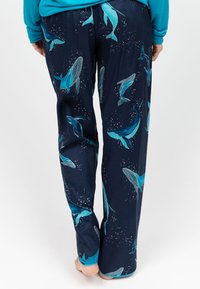 Donkerblauwe pyjamabroek met een walvispatroon in turquoise en lichtblauw. Wijde pijpen, zachte textuur en een elastische tailleband.