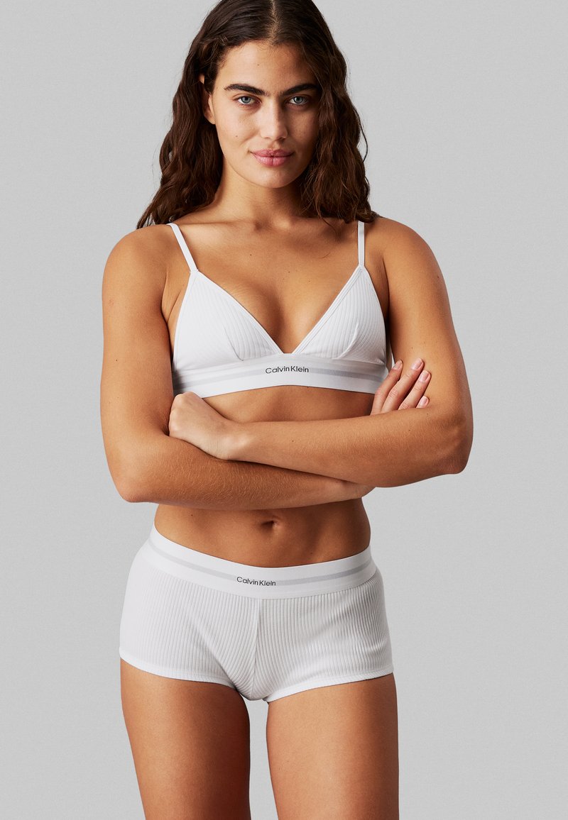 Bijela rebrasta braletka i gaće s kratkim nogavicama, s Calvin Klein logotipom, s tankim naramenicama i pojasom, glatke teksture i prilagođenog dizajna.