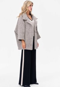 Grijze wolmix oversized jas met een een textuurafwerking, grote notch-kraag en twee knopen, gecombineerd met zwarte wijde pantalons met witte strepen.