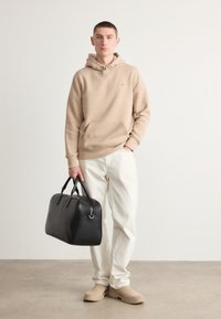 Beige hoodie with a front pocket, light-colored jeans, beige slip-on shoes, and a black leather bag with dual handles.