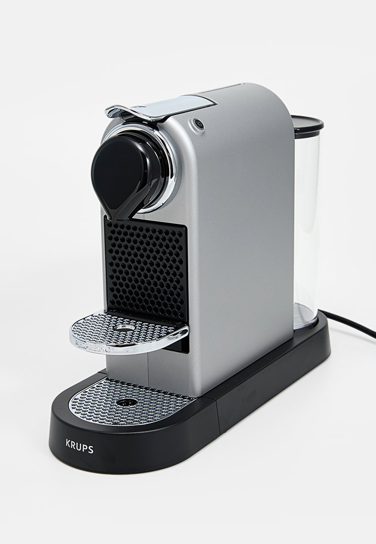 Machine à café à portion individuelle avec un corps en argent élégant, des accents noirs, un plateau d'égouttage texturé et un réservoir d'eau transparent.