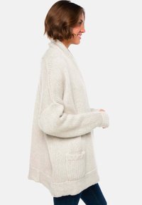 Cardigan en maille surdimensionné beige clair avec une finition texturée, à ouverture frontale, manches raglan et détail de poche à l'avant.