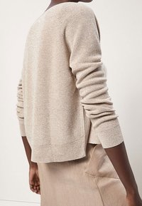 Maglione beige a maglia con un fit rilassato, caratterizzato da maniche lunghe, una leggera lucentezza e un ampio scollo. Abbinato a una gonna coordinata.