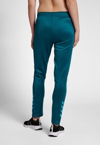 Teal sportieve joggers met een taps toelopende pasvorm, voorzien van een trekkoord in de taille en zijstrepen. Gecombineerd met zwarte schoenen en een textuurstof.