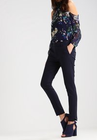 Marinblomstrig blus med kall-skulder design; lätt och genomskinligt tyg. Kombinerad med skräddarsydda svarta byxor och marinblå klacksandaler.