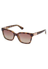 Gafas de sol carey con un diseño cuadrado, lentes degradados y herrajes en tono dorado con un patrón geométrico en las patillas.