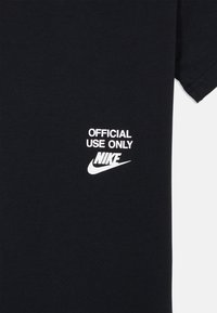 Juodas medvilninis marškinėliai su baltais spaudiniais "OFFICIAL USE ONLY" ir Nike logotipu. Apvalus kaklas ir trumpomis rankovėmis. Lygus paviršius.