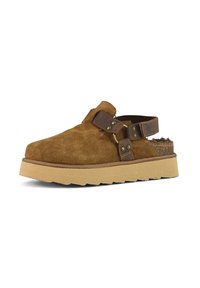 Scarpa slip-on scamosciata marrone con suola beige chunky, dotata di fascette in pelle marrone e accentuazioni in metallo. Parte superiore testurizzata e rivestimento imbottito.