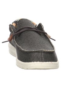 Scarpa slip-on nera in tessuto intrecciato con parte superiore testurizzata, suola in gomma bianca, cuciture a contrasto e lacci marroni. Dettaglio di fodera interna con motivo.