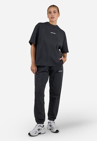 T-shirt noir gris surdimensionné à manches courtes et logo, associé à un jogging assorti. Le tissu semble doux avec des poignets élastiqués.