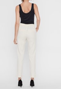 Krämfärgade avsmalnande byxor med elastisk midja och sidofickor, kombinerat med en svart linne och svarta högklackade skor.