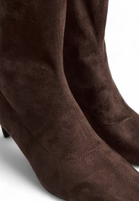 Bottines en daim marron avec un bout effilé et un talon bas. Surface texturée avec des détails de couture visibles, mettant en valeur un design épuré.