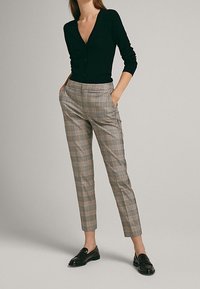 Cardigan noir à col en V, associé à un pantalon à carreaux beige ajusté. Mocassins noirs complètent la tenue. Design simple et ajusté.