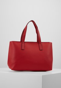 Červená kabelka z texturované kůže se dvěma krátkými uchy, strukturovaným tvarem a minimem švů. Hladký vnitřek, bez ozdob.