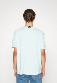 Světle modré tričko s krátkým rukávem vyrobené z měkké bavlny s kulatým výstřihem, na zadní straně se viditelnou štítkovou logem a uvolněným střihem.