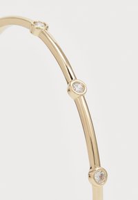 Gold-tone metal bangle with a smooth, curved design, featuring clear, round gemstones evenly spaced along the band.