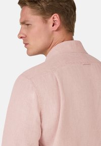 Camicia in lino rosa chiaro con colletto, caratterizzata da una consistenza sottile. Sul retro presenta un piccolo asola e una cura nei dettagli della cucitura.