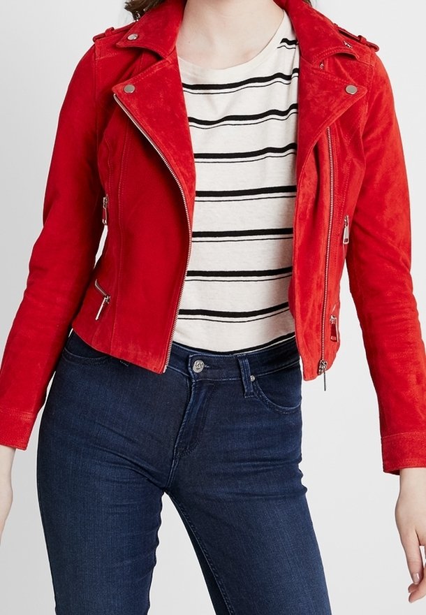 Giacca da motociclista in suede rosso con tasche con cerniera, colletto con bottone a pressione e design aderente, indossata sopra una maglia a righe e abbinata a jeans scuri.