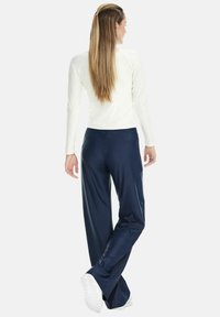 Light ivory long-sleeve top paired with navy, loose-fitting pants. Smooth fabric texture; pants feature a subtle flare at the cuffs.