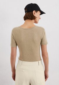 Korte mouwen, beige top van zachte stof, met een ronde halslijn en een subtiele textuur, gecombineerd met hooggetailleerde, lichtgekleurde broeken.