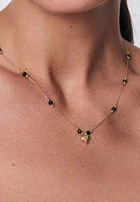 Złoty naszyjnik z łańcuszka z czarnymi koralikami, z sercowym wisiorkiem. Delikatny design, gładka tekstura i wysokiej jakości rzemiosło.