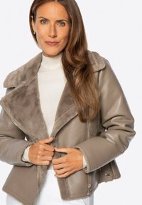 Taupe leren jack met een nepbont kraag, ritszakken en een getailleerd ontwerp, met een zachte textuur en contrasterende binnenvoering.