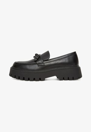 Mocasines de cuero negro con suela plataforma, con un lazo decorativo en la parte delantera y un diseño de tracción prominente en la suela.