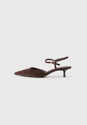 Chaussure slingback en daim marron à bout pointu, avec un petit talon kitten et une bride de cheville ajustable avec une boucle dorée, sur un fond gris uni.