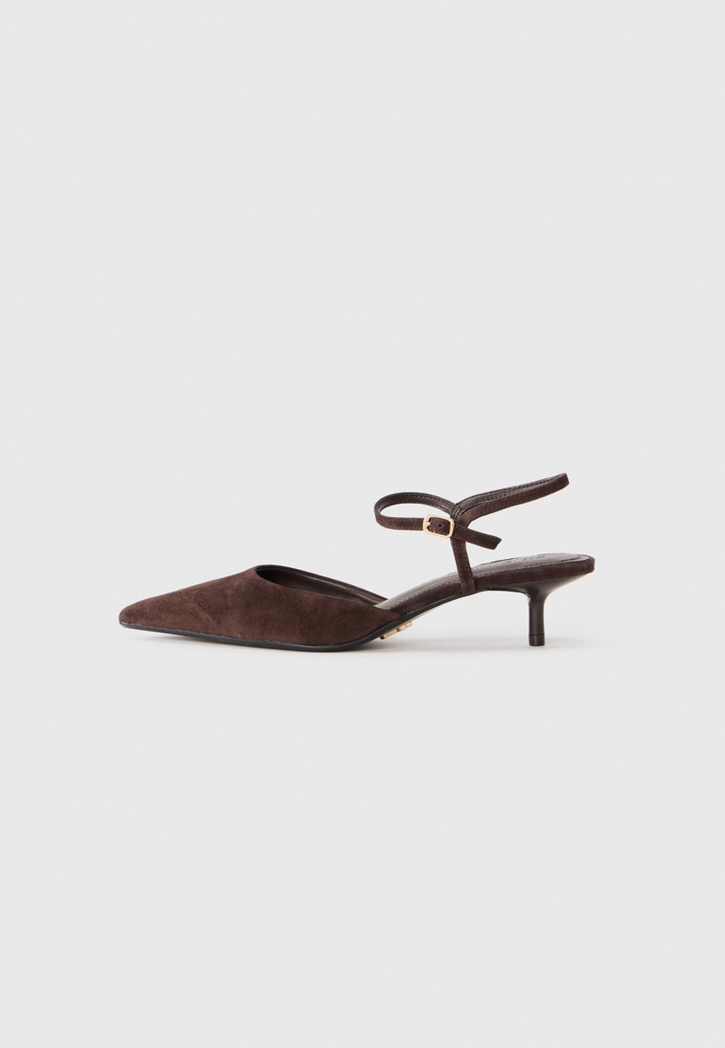 Chaussure slingback en daim marron à bout pointu, avec un petit talon kitten et une bride de cheville ajustable avec une boucle dorée, sur un fond gris uni.