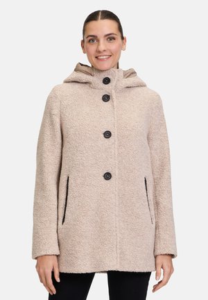 Beige strukturierter Mantel mit Kapuze, fünf schwarzen Knöpfen und Seitentaschen. Der Stoff wirkt weich und flauschig und hat einen lässigen, oversized Schnitt.