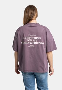 Paarse, oversized katoenen t-shirt met korte mouwen en witte tekst op de achterkant met de tekst "Alles voor mijn Familie & Vrienden."