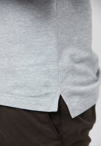 Szara bawełniana koszula o fakturowanym wykończeniu, z bocznymi rozporkami u dołu oraz subtelnym detalem z logo w pobliżu szwu.