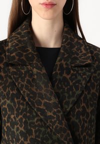 Manteau à imprimé léopard en vert foncé et marron, fabriqué en tissu texturé, avec un large col et un design double boutonnage.
