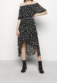 Schwarzes schulterfreies Kleid mit weißem Blumenmuster, geschichteten Rüschen und asymmetrischem Saum. Kombiniert mit schwarzen Schnürstiefeletten.